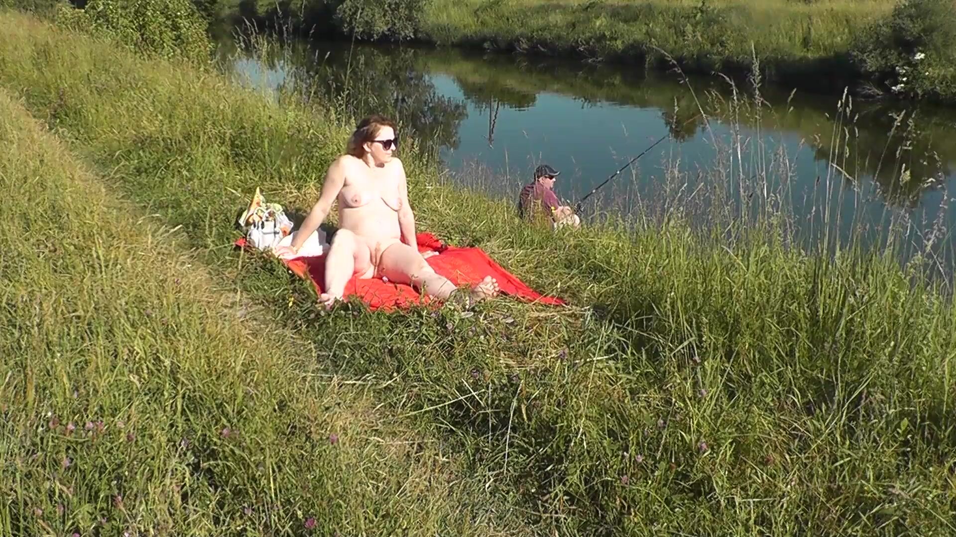 MILF sexy Frina na margem do rio despida e a apanhar banhos de sol nua. Um  pescador aleatório observa-a, e no final decide juntar-se à mulher nua.  Praia selvagem. Praia de nudismo.